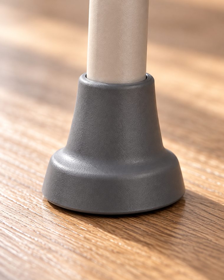 Close-up of a telescoping leg: the inner tube with its row of adjustment holes, ending in a wide grey rubber foot flat against the wood floor.